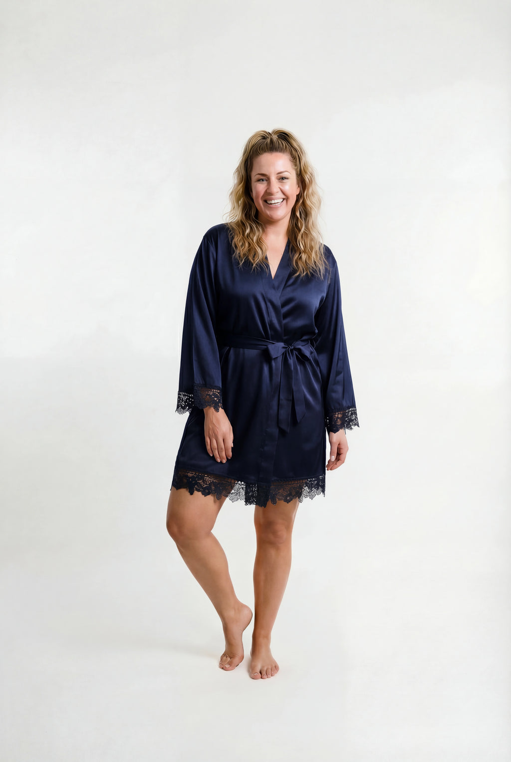 Woman wearing a navy blue satin robe with lace trim on a white background